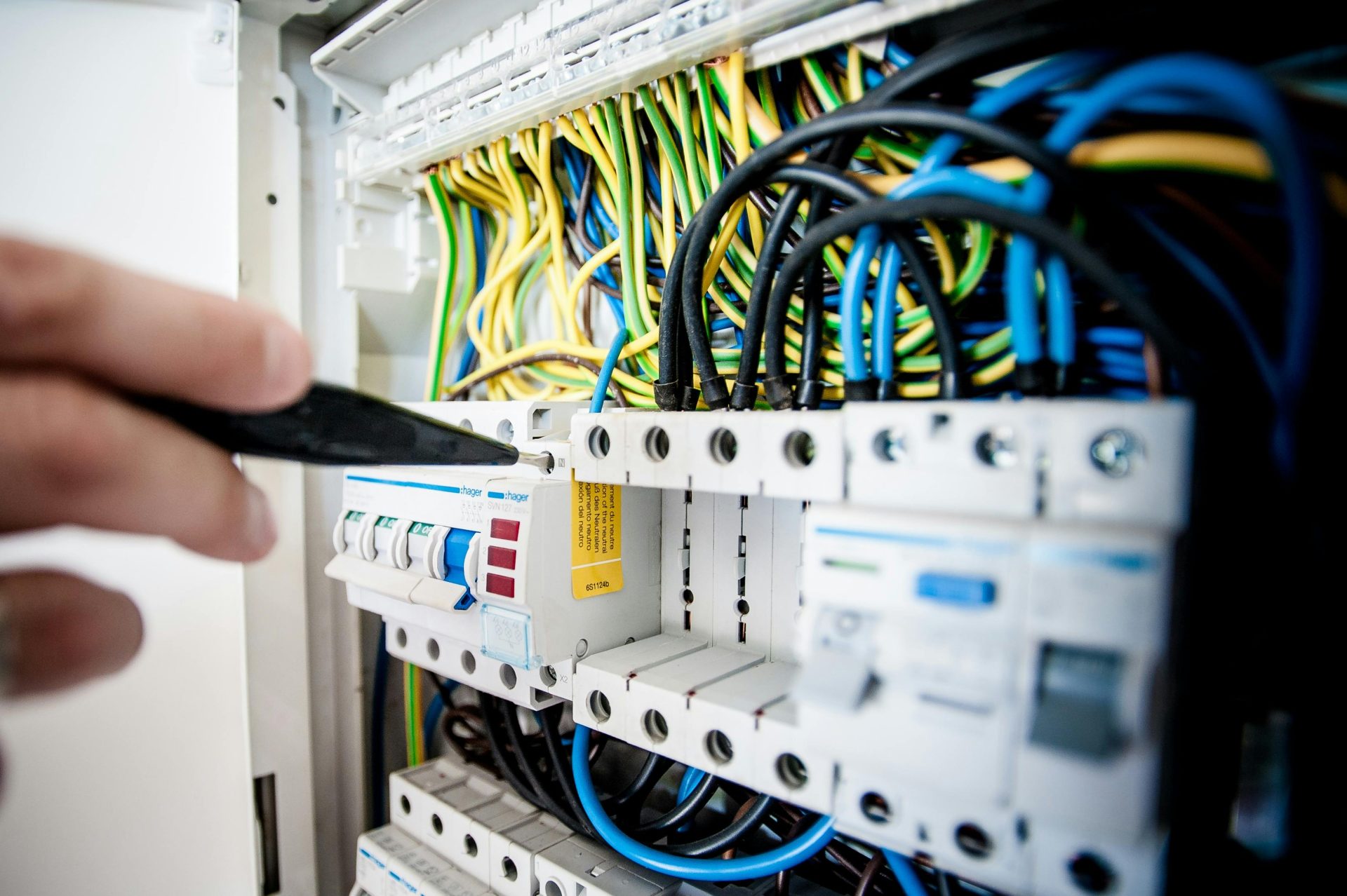 Mano de electricista trabajando en un panel de disyuntores con cables de colores, garantizando conexiones eléctricas seguras.