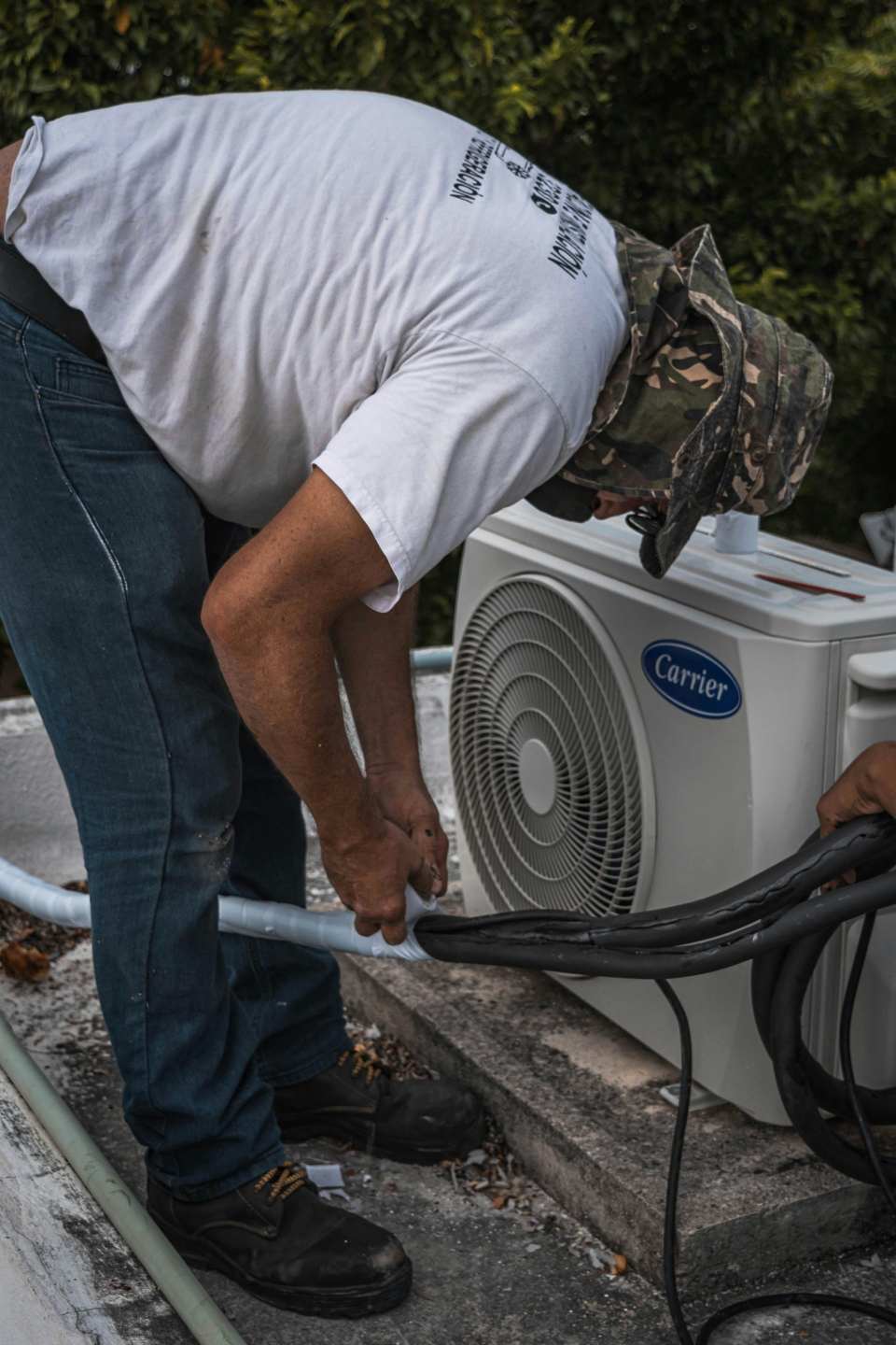 Un técnico realiza mantenimiento en una unidad de aire acondicionado exterior, centrándose en las conexiones de las mangueras.
