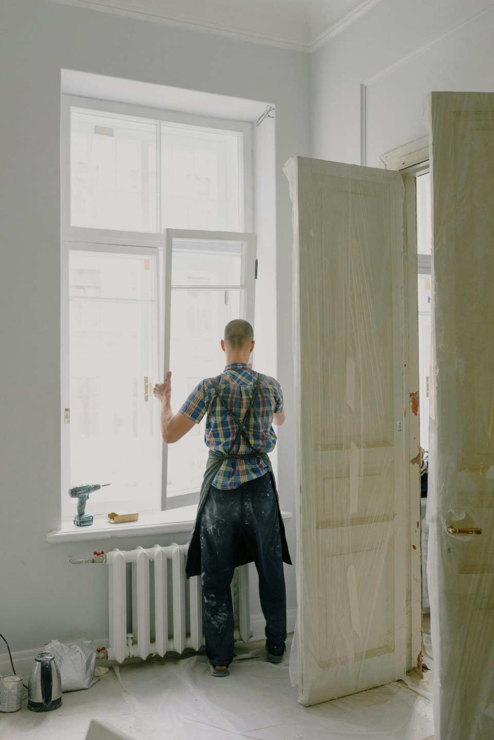 Vista de cuerpo entero de un manitas arreglando una ventana moderna en una habitación luminosa.