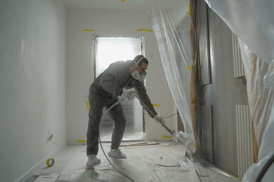 Un trabajador con equipo de protección pintando paredes durante un proyecto de renovación de interiores.
