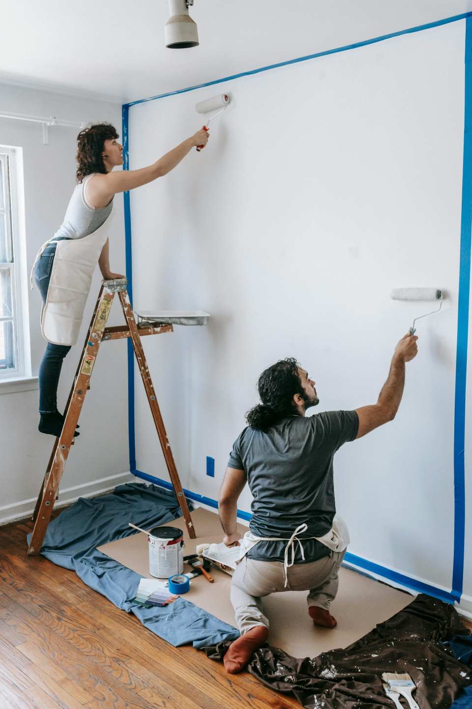 Una pareja colabora pintando una pared blanca en su nuevo hogar, demostrando trabajo en equipo y renovación.